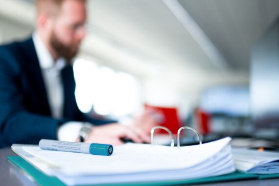 aufgeschlagener Ordner befindet sich auf einem Tisch, darauf liegt ein Stift