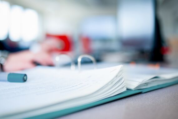 aufgeschlagener Ordner liegt auf dem Tisch, darauf liegt ein Stift