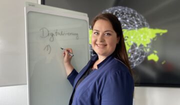 Frau steht vor einer Tafel, auf der das Wort Digitalisierung steht