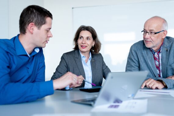 Zwei Männer und eine Frau sitzen zusammen und erarbeiten Strategien zur Konfliktbewältigung